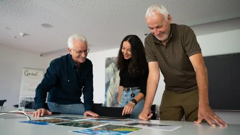 Drei Personen betrachten Bilder auf einem Tisch.