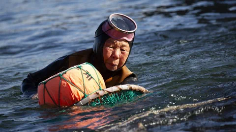 Ältere Taucherin mit Ausrüstung im Meer schwimmend.