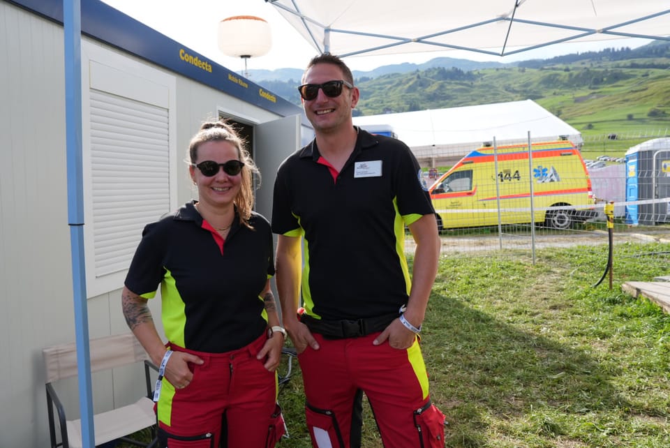 Zwei Rettungssanitäter in Uniform vor einem Zelt und einem Krankenwagen am Open Air Lumnezia 2024 in Degen.