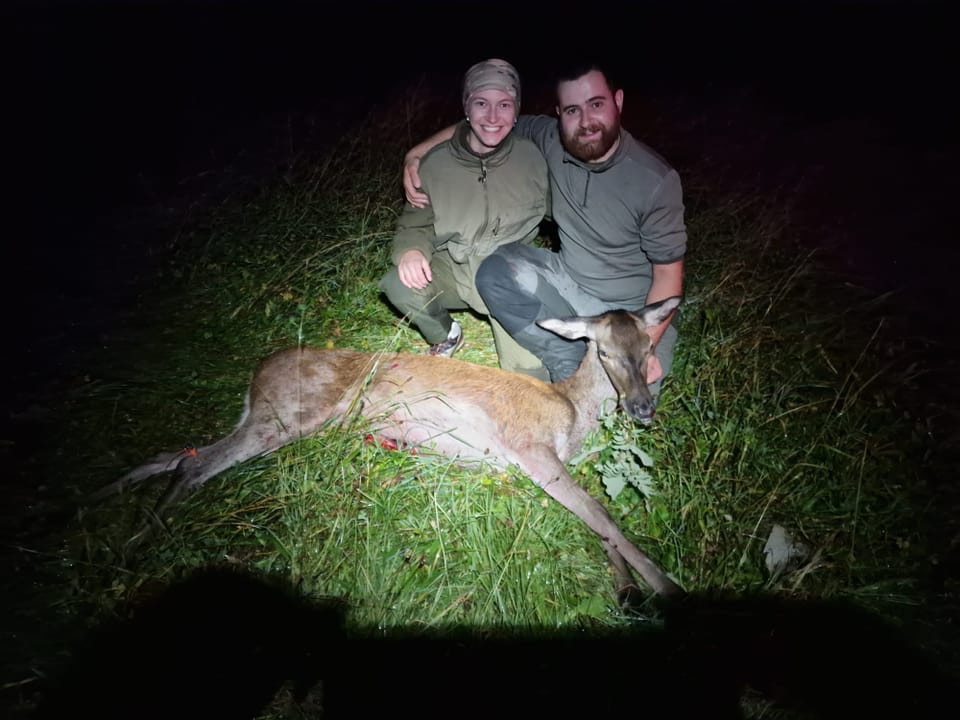 Zwei Menschen neben einem toten Hirsch im Gras in der Nacht.