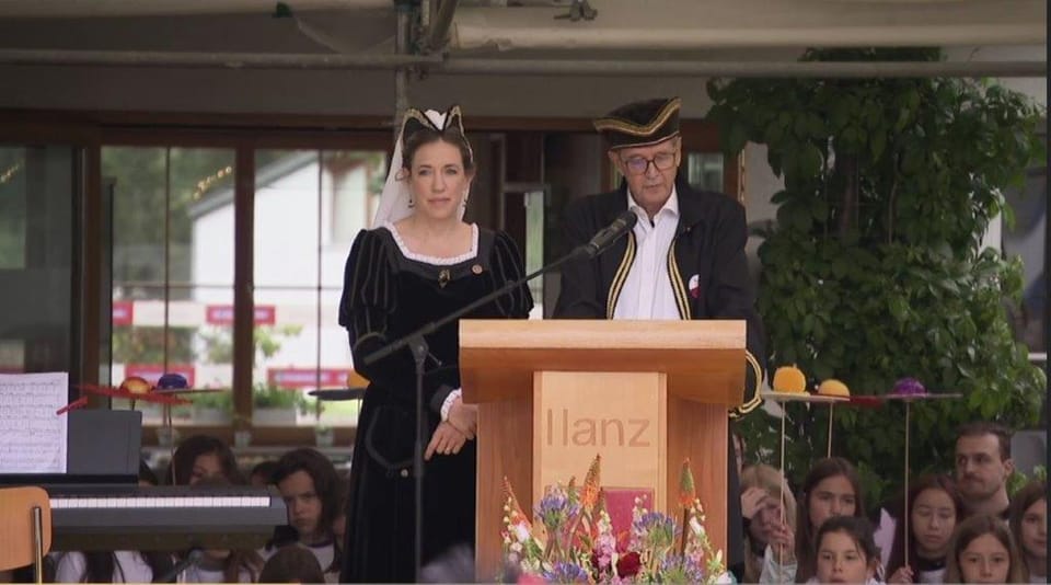 Rednerpult in Ilanz mit Rednern in traditioneller Kleidung vor Publikum.