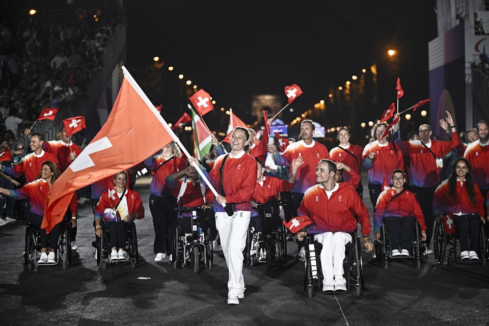 Schweizer Athleten im Rollstuhl schwenken Flaggen bei einer Parade.