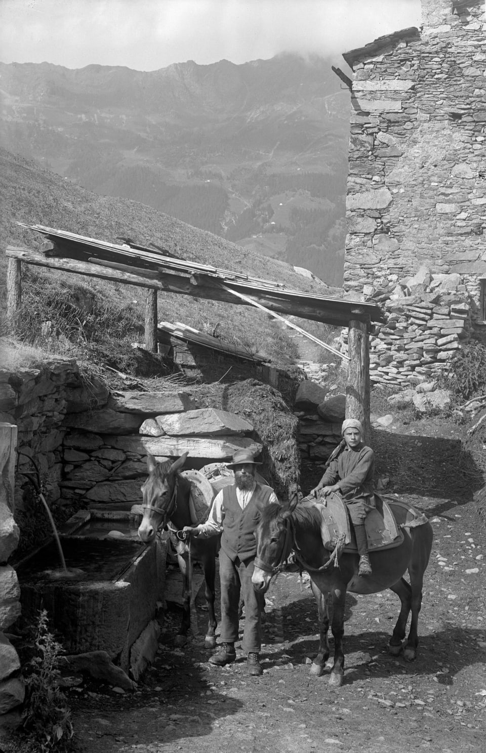 Zwei Männer mit Pferden vor einer Steinmauer in den Bergen.