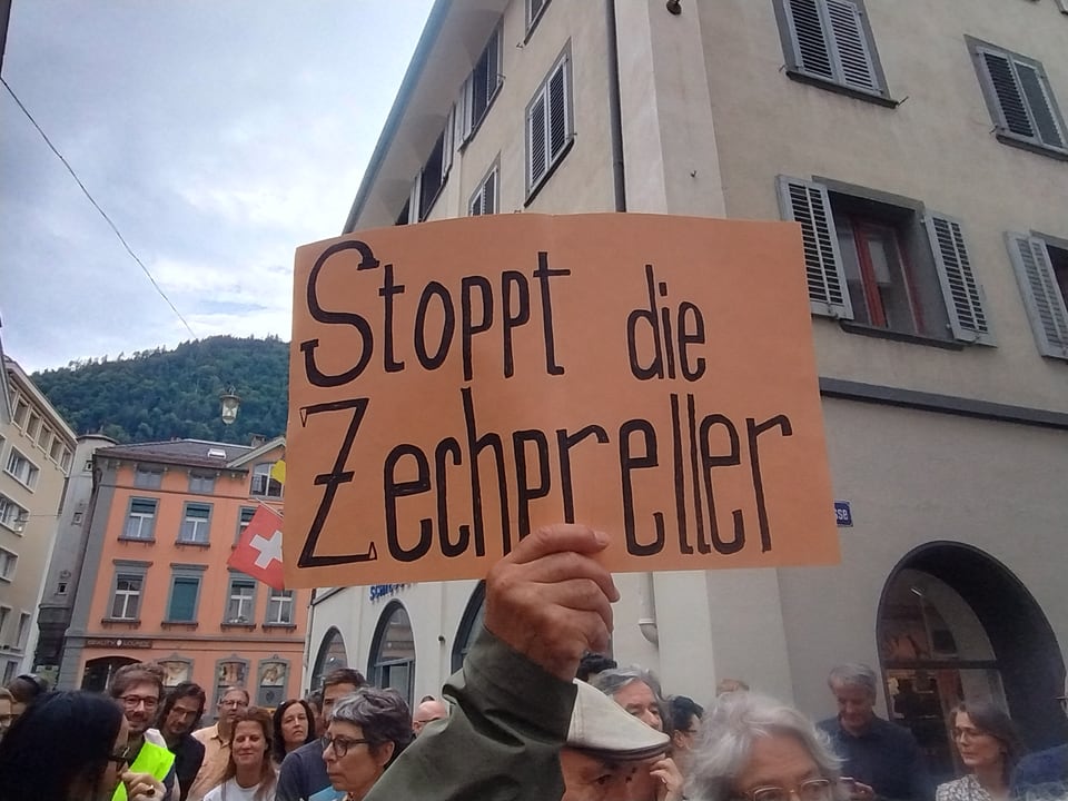 Protestierende halten ein Schild mit der Aufschrift 'Stoppt die Zechpreller' in einer Innenstadt.