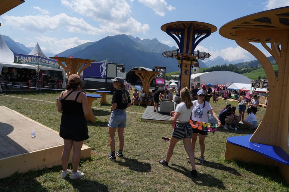 Menschen auf einem Outdoor-Festivalgelände mit Bergen im Hintergrund am Open Air Lumnezia 2024.