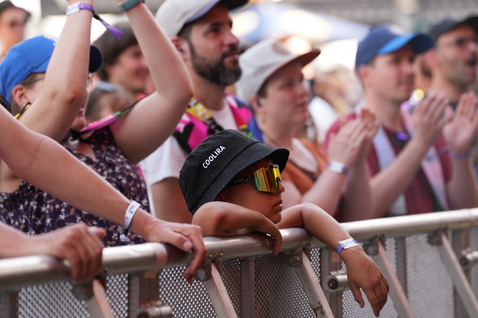 Kind mit Sonnenbrille lehnt sich bei einem Konzert an die Absperrung am Open Air Lumnezia 2024.