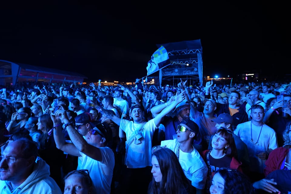 Menschenmenge bei einem Nachtkonzert unter blauem Licht am Open Air Lumnezia 2024.