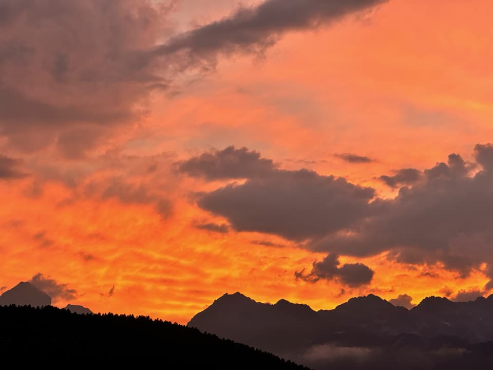 Wolken über den Bergen in Rotlicht getaucht.