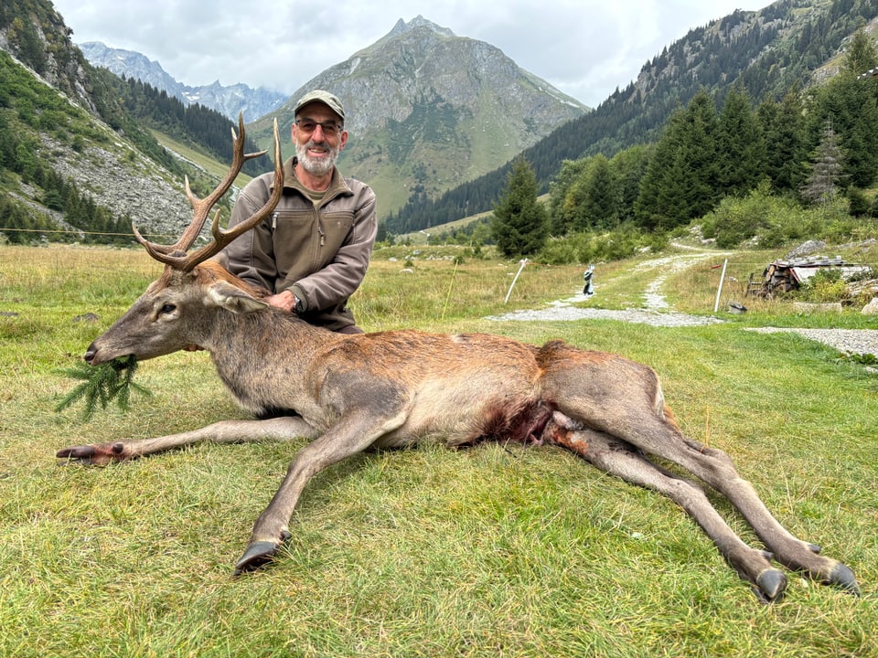 Mann posiert in den Bergen mit erlegtem Hirsch.