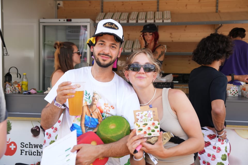 Zwei Personen halten Obst und Getränke auf einem Marktstand am Open Air Lumnezia 2024.
