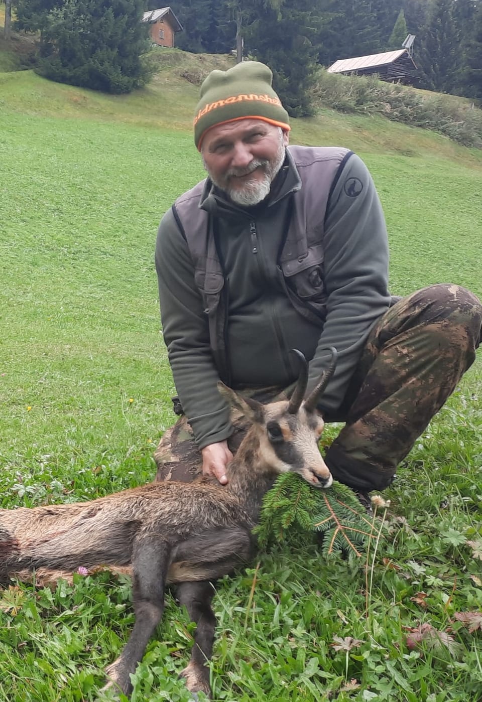 Mann mit erlegtem Wildtier auf einer Wiese.