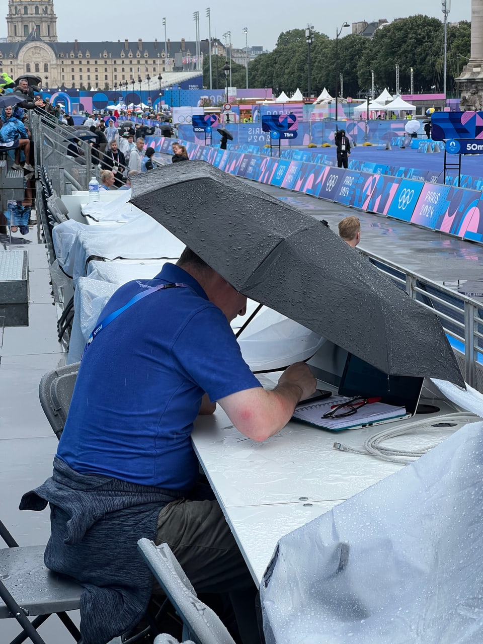 Paris 2024: Journalist unter einem Regenschirm.