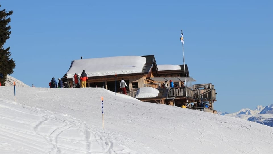 Berghütte im Schnee mit Menschen und blauen Himmel.