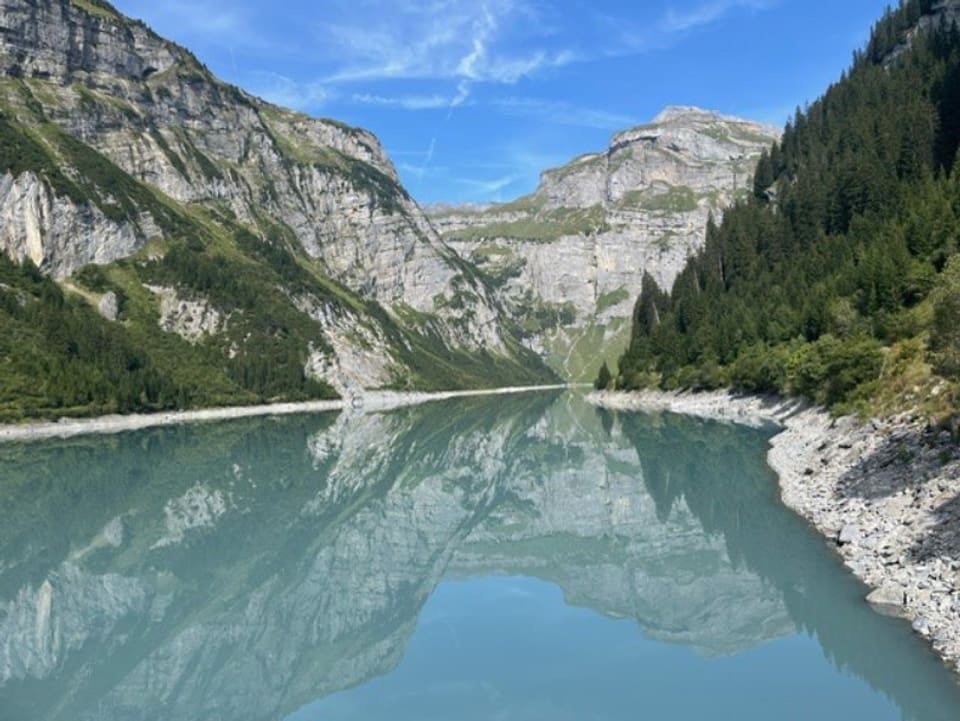 Bergsee mit Spiegelung, umgeben von Bergen und Wald.