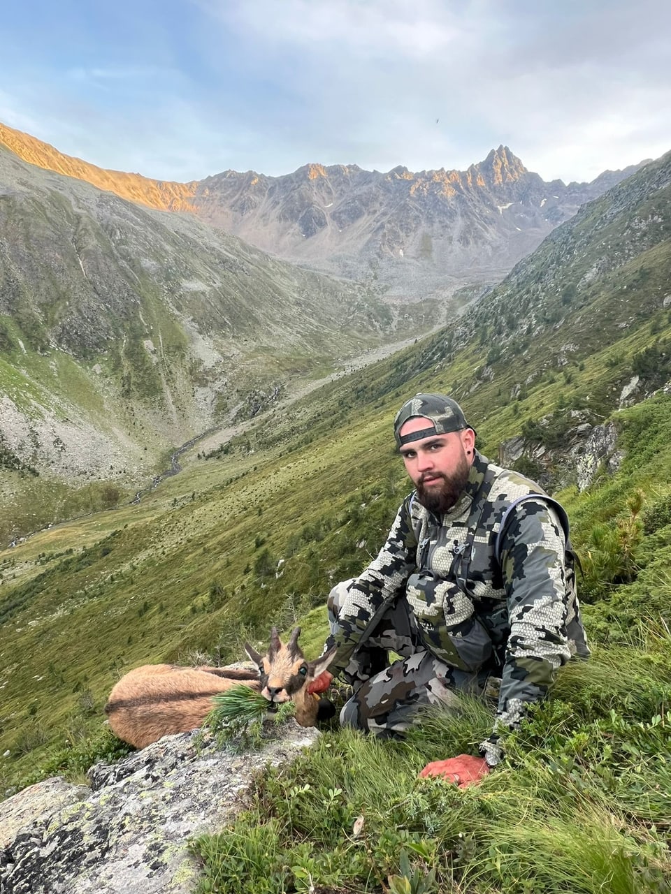 Jäger in Tarnkleidung mit erlegtem Steinbock in den Alpen.