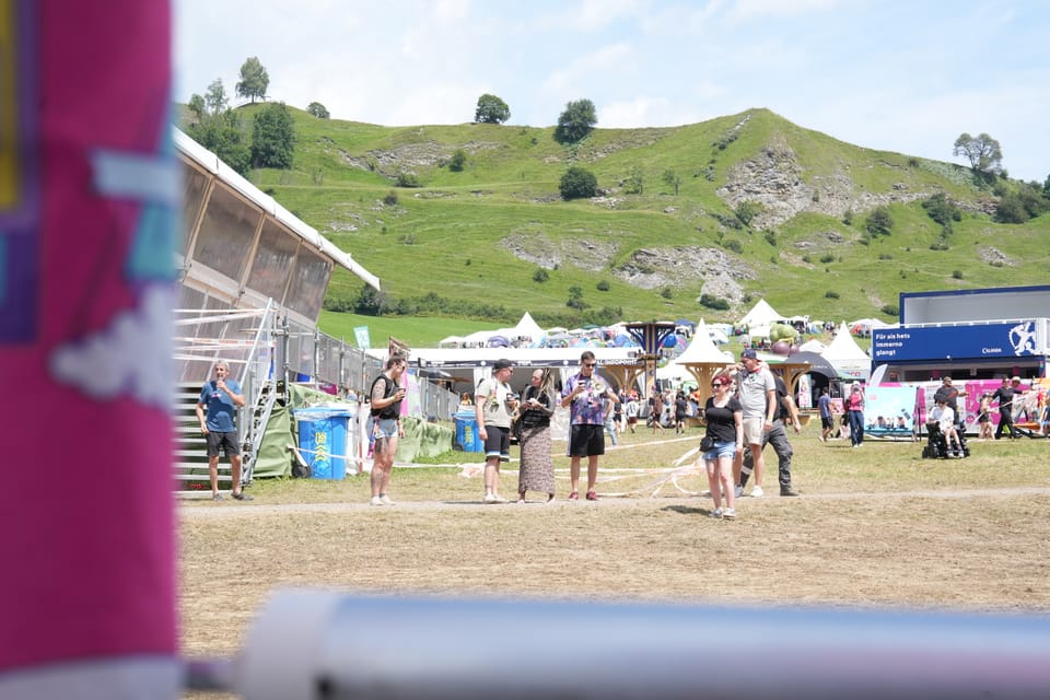 Menschen auf einem Festivalgelände vor Hügeln am Open Air Lumnezia 2024 in Degen.