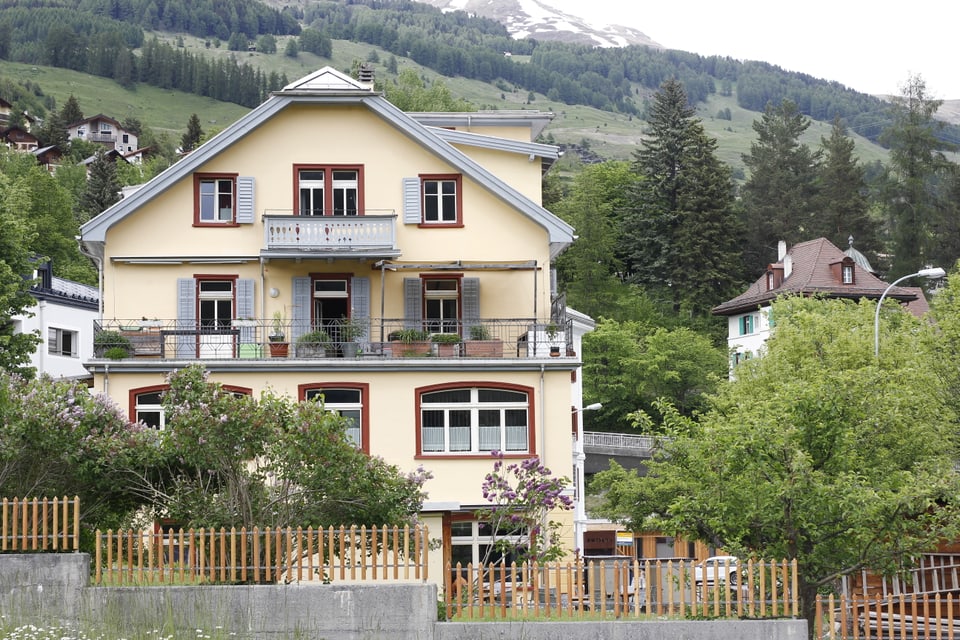 Movimento Scuol: Gelbes Haus in alpiner Landschaft vor bewaldetem Hügel.