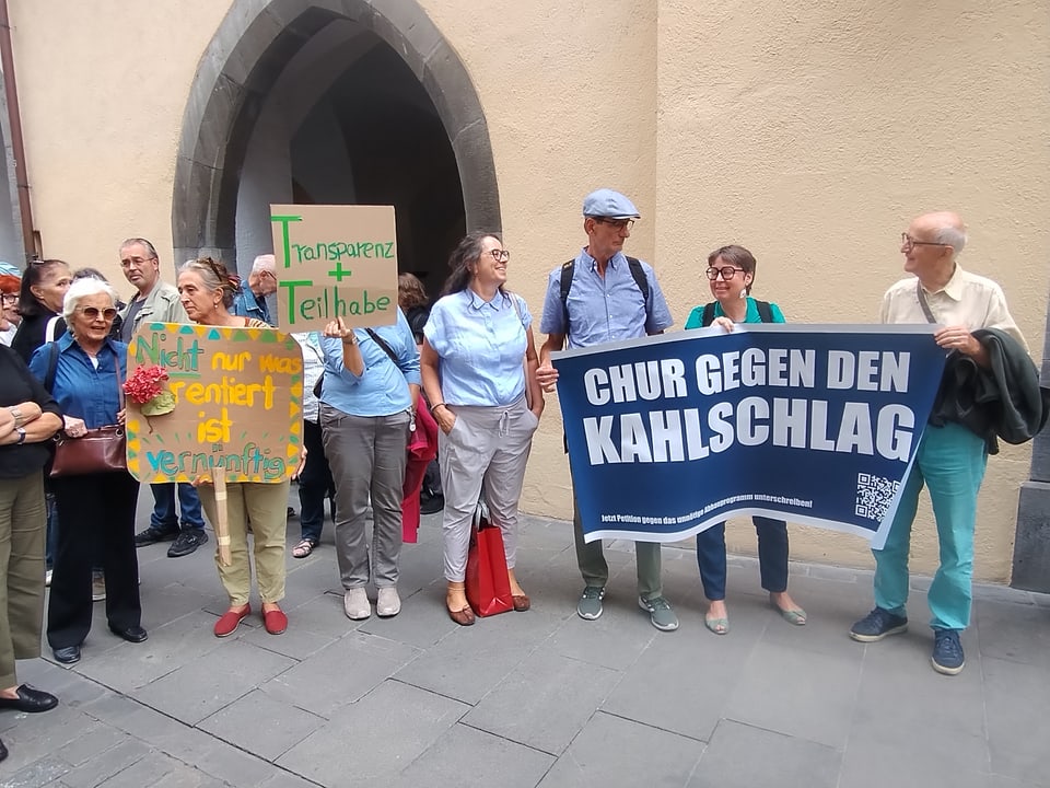 Menschen halten Protestschilder vor einem Gebäude.