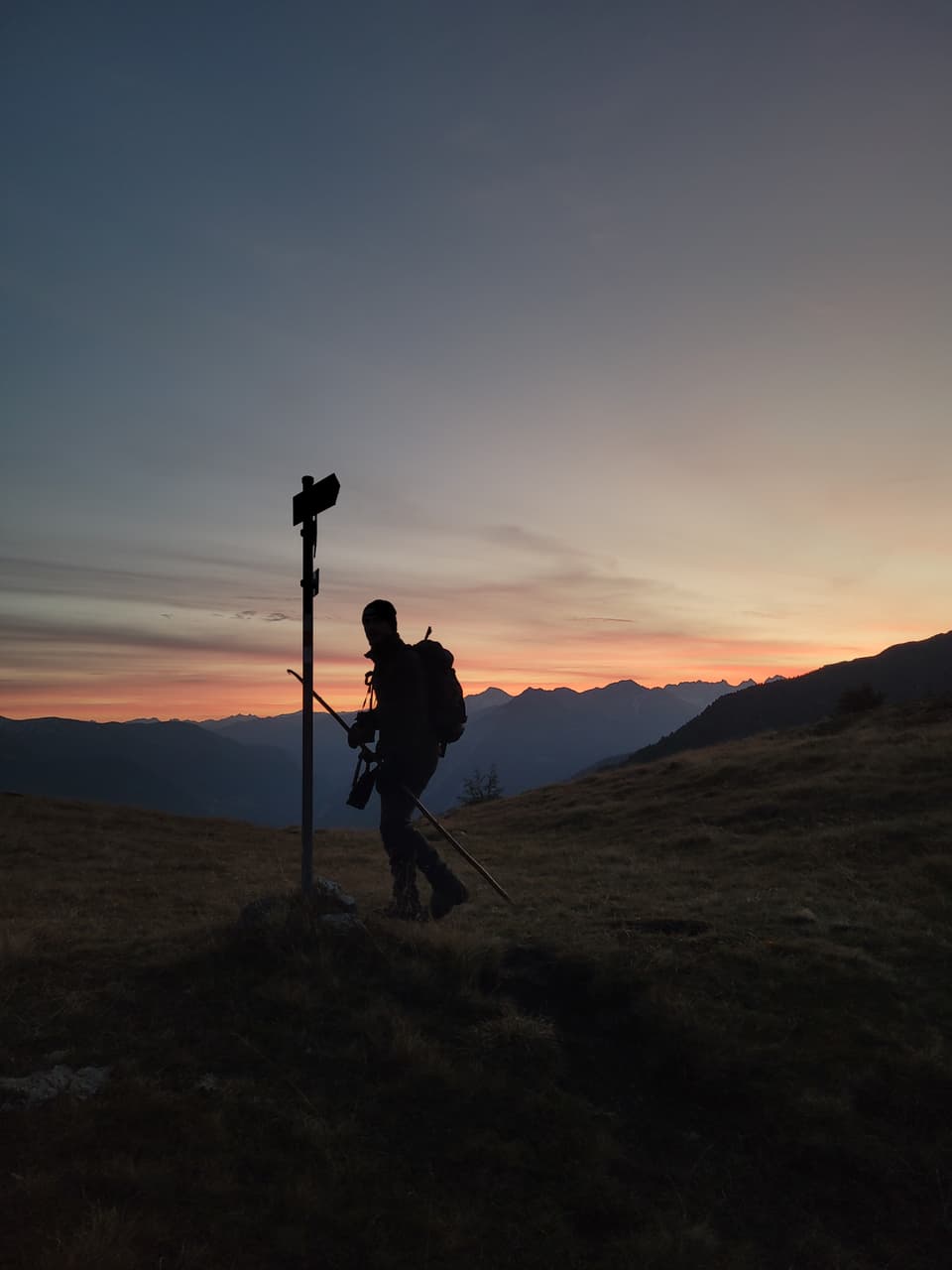 Wanderer bei Sonnenuntergang auf Berg mit Wegweiser.