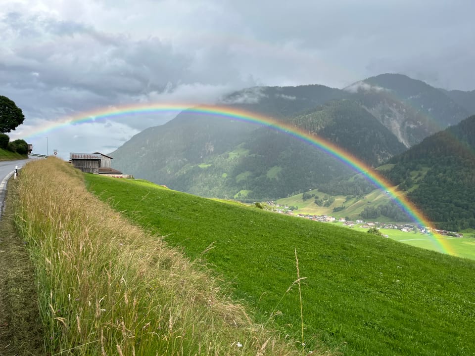 Regenbogen über einer grünen Landschaft mit Hügeln.