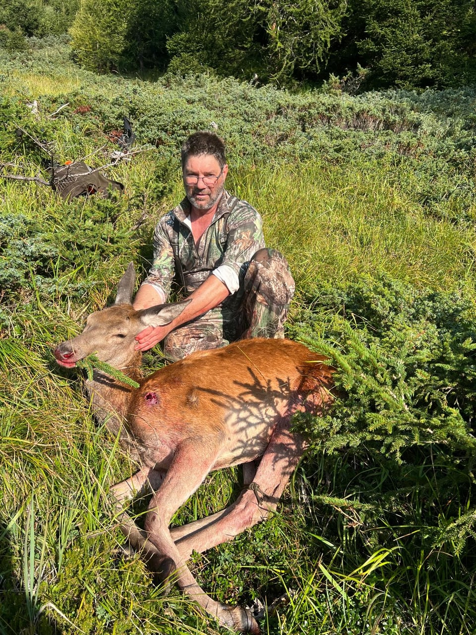 Jäger mit erlegtem Hirsch im Gras.