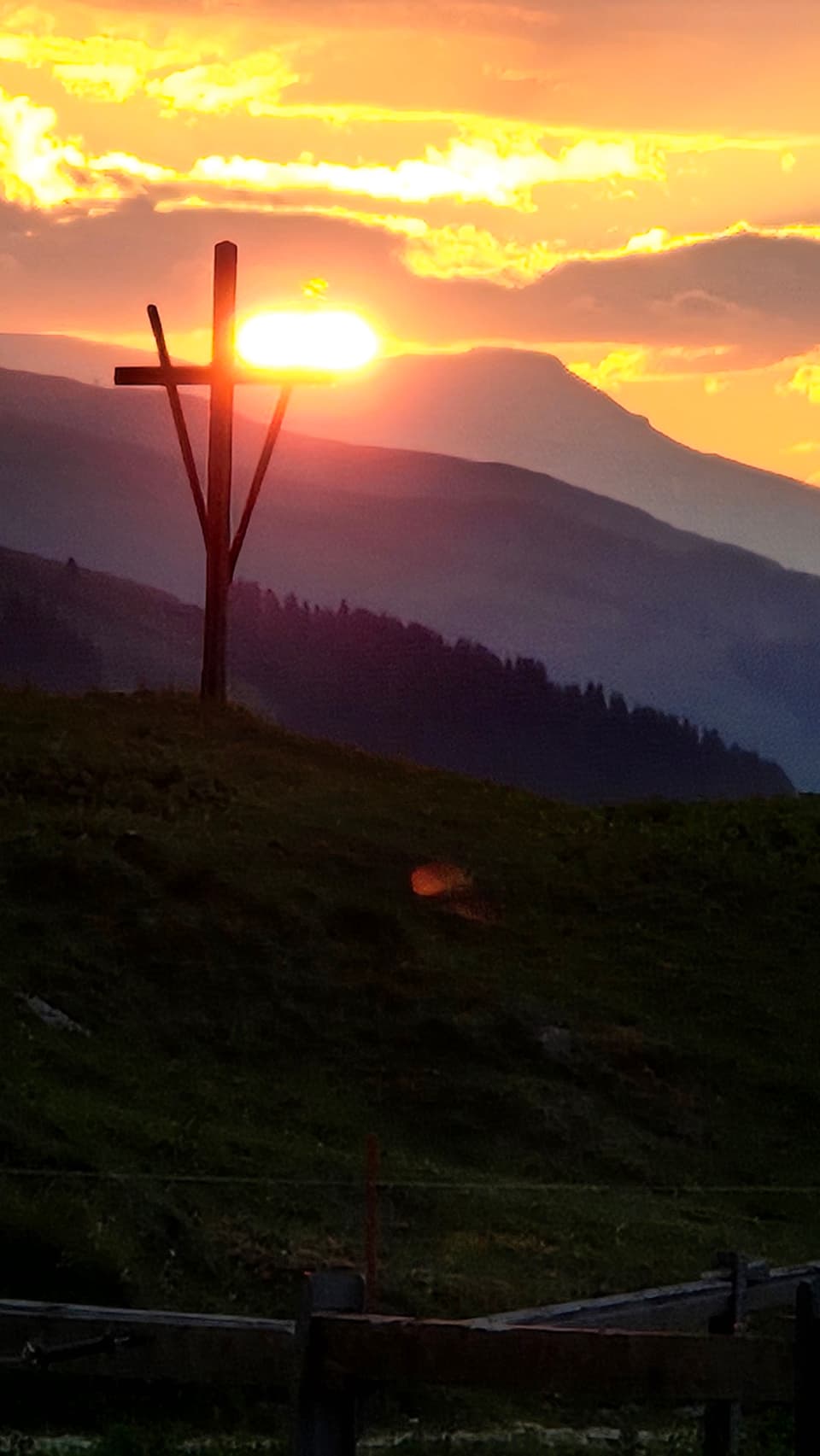 Holzkreuz auf einem Hügel bei Sonnenuntergang.