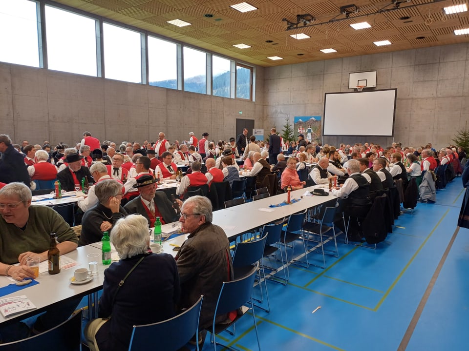 Jodler/Innen in einer Turnhalle beim Mittagessen