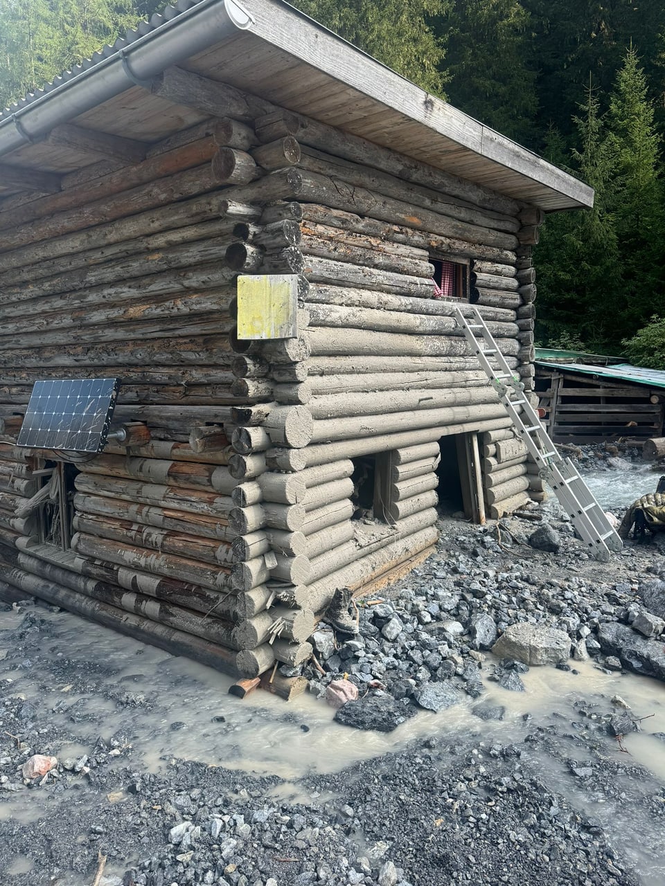 Blockhütte aus Holzstämmen mit Schlamm und Schutt umgeben.