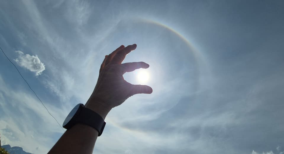 Hand, die vor einem Sonnenhalo im Himmel gehalten wird.