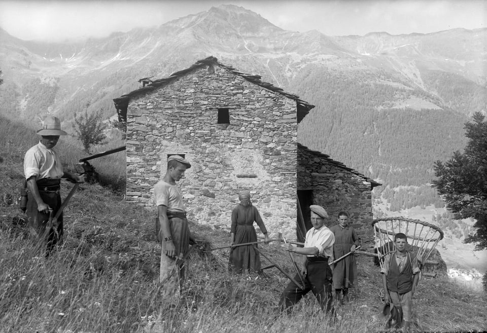 Bauern bei der Feldarbeit vor einem alten Steinhaus in den Bergen.