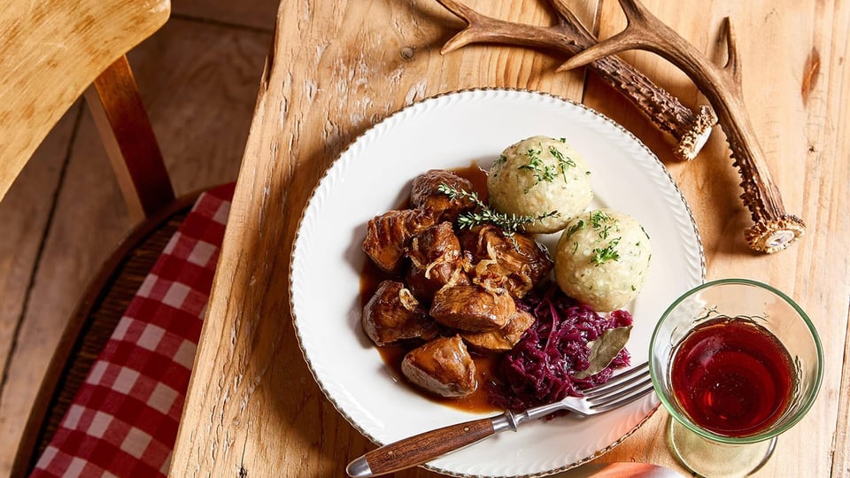 Ein Teller mit Fleisch, Knödeln, Rotkohl und einem Glas Rotwein.