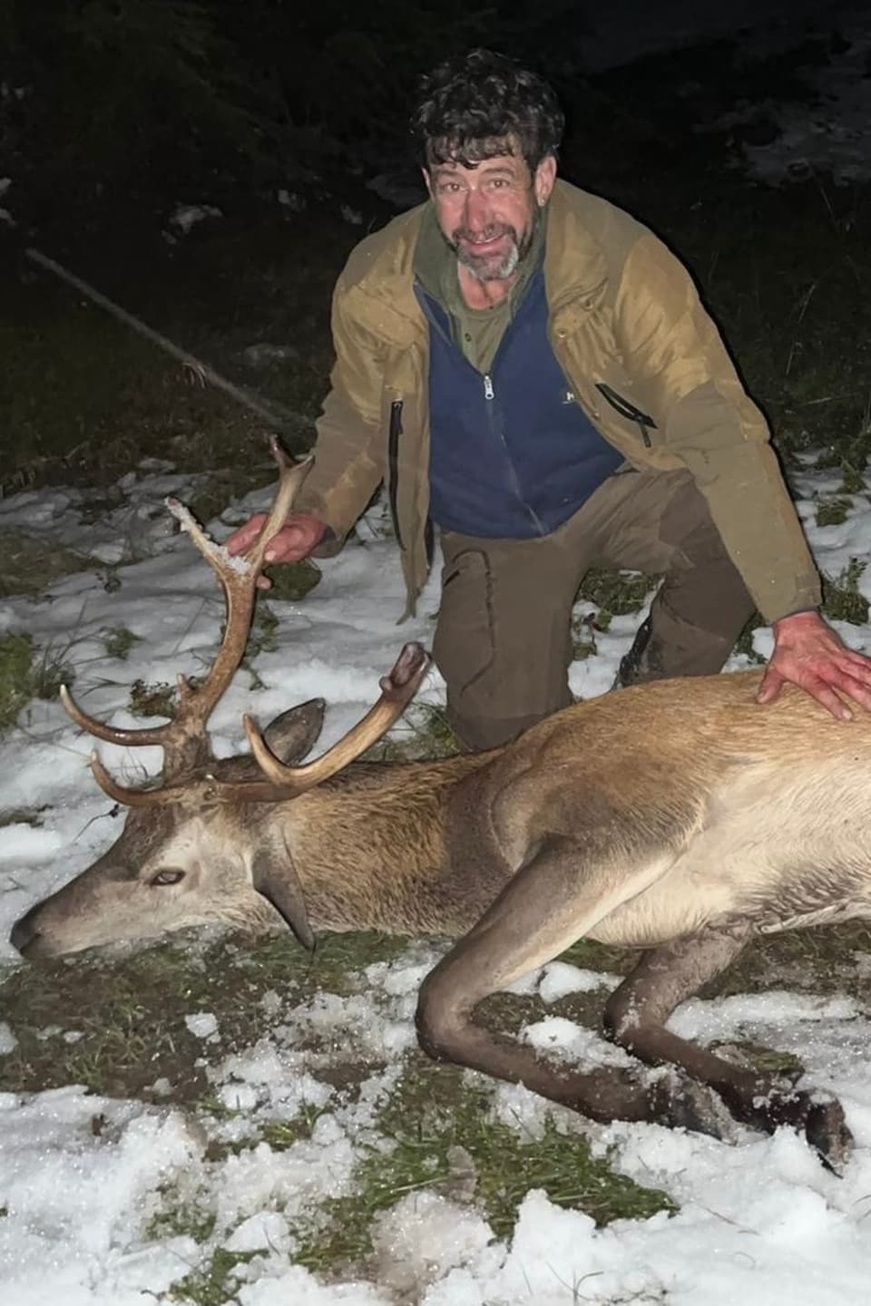 Mann neben erlegtem Hirsch im Schnee.