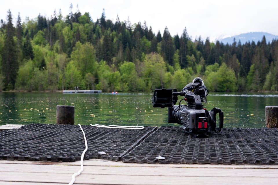 Videokamera auf dem Steg am See vor einem bewaldeten Hintergrund.