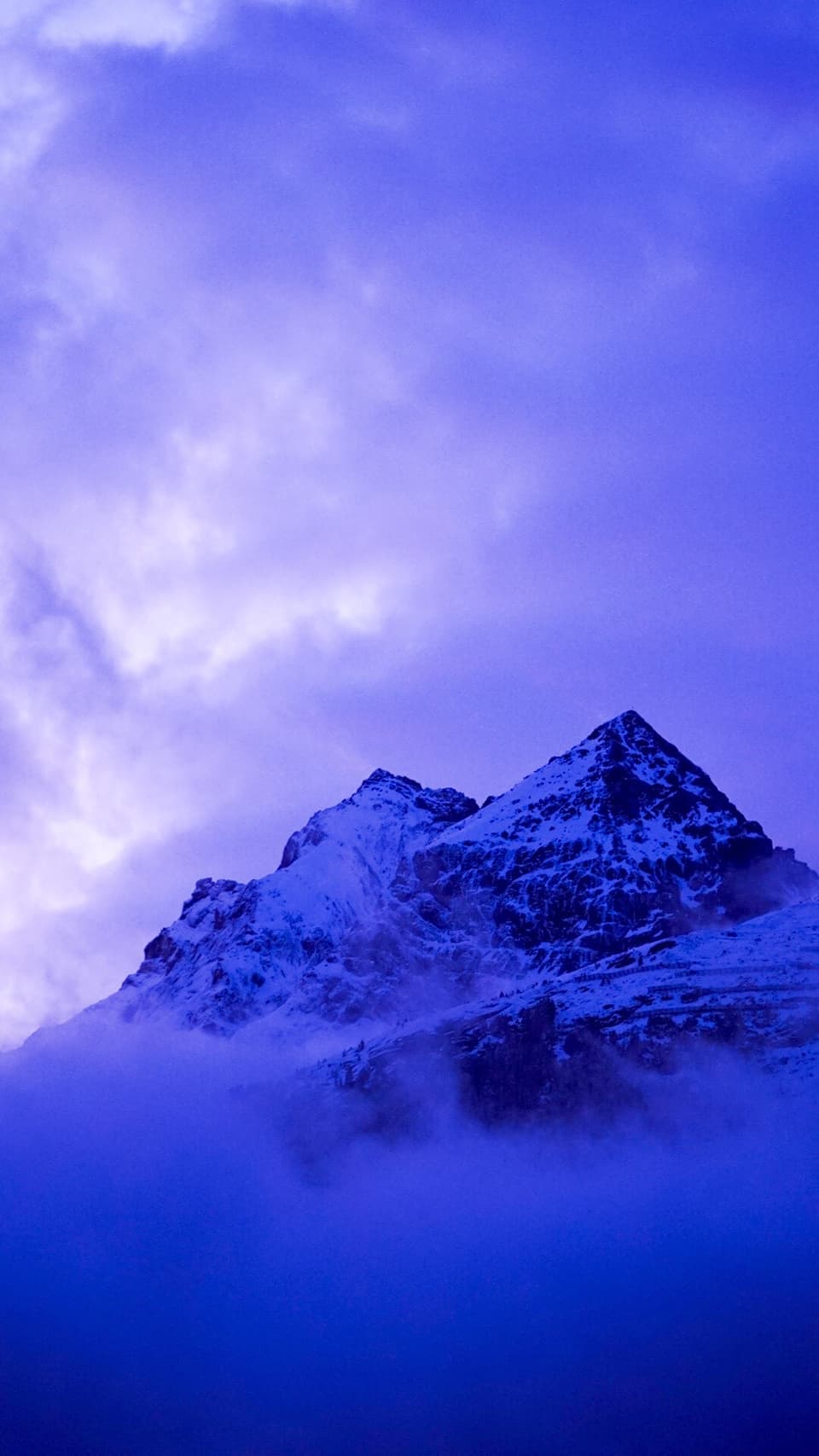 Schneebedeckter Berggipfel in blauer Dämmerung.