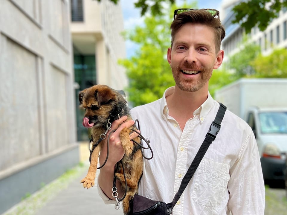 Mann lächelt und hält Hund auf dem Arm, auf städtischer Strasse.