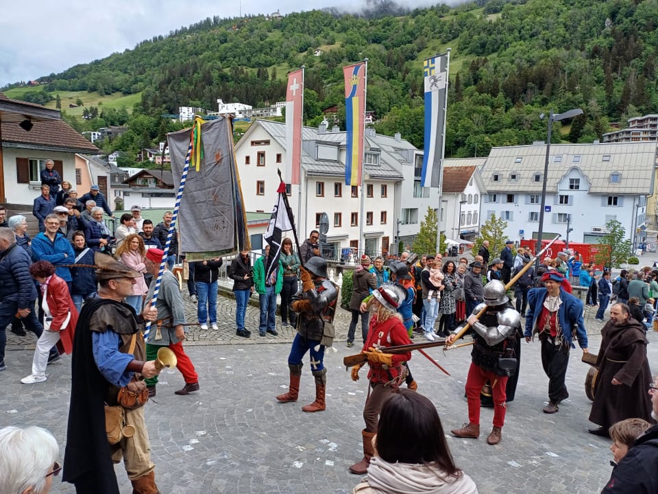 Mittelalterliche Kostümparade auf einer Strasse mit Publikum und Fahnen.