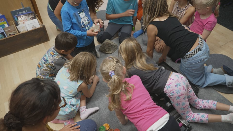 Die Kinder beugen sich im Schulzimmer über die gefundenen Kristalle.