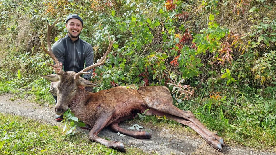 Mann posiert neben einem erlegten Hirsch in der Natur.