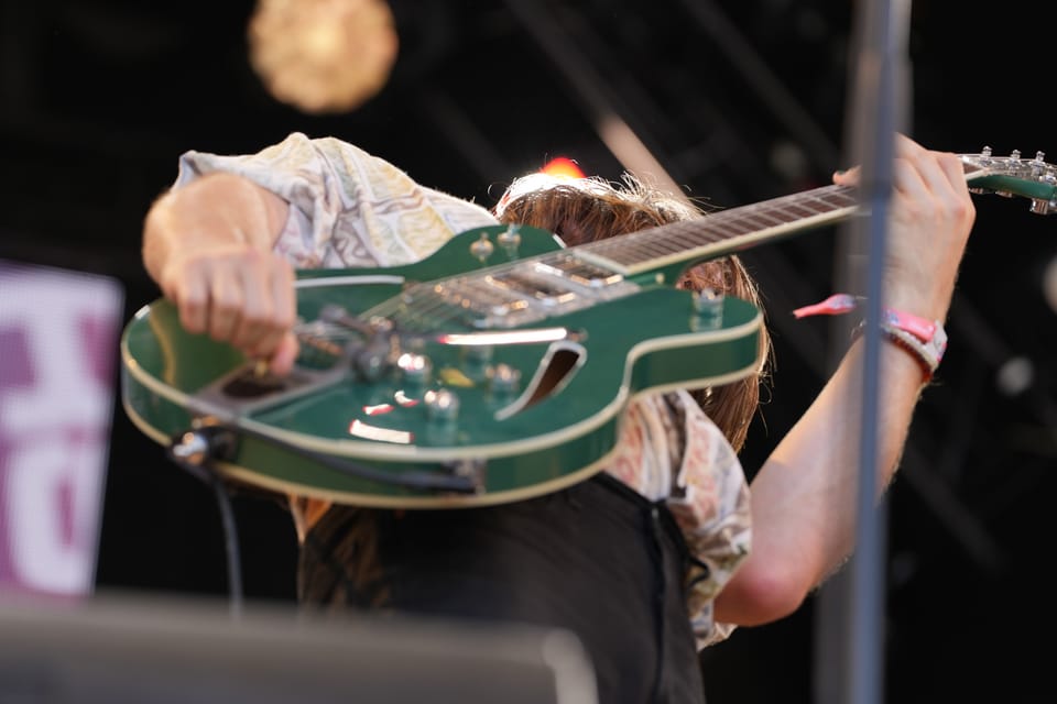 Musiker hält grüne E-Gitarre auf der Bühne hoch am Open Air Lumnezia 2024.