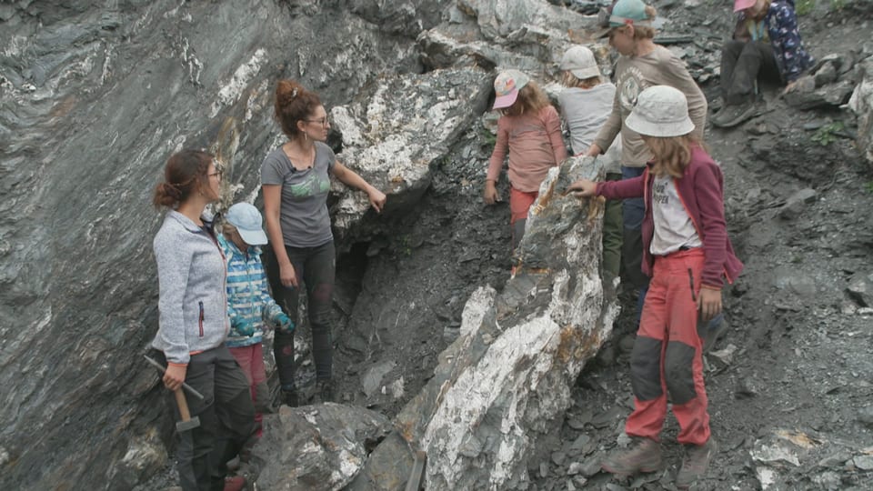 Die Kinder stehen vor einem Felsen und suchen Kristalle. 