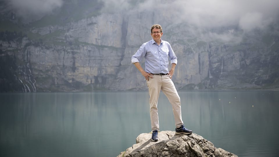 Albert Rösti auf Felsen am See mit Berglandschaft im Hintergrund.