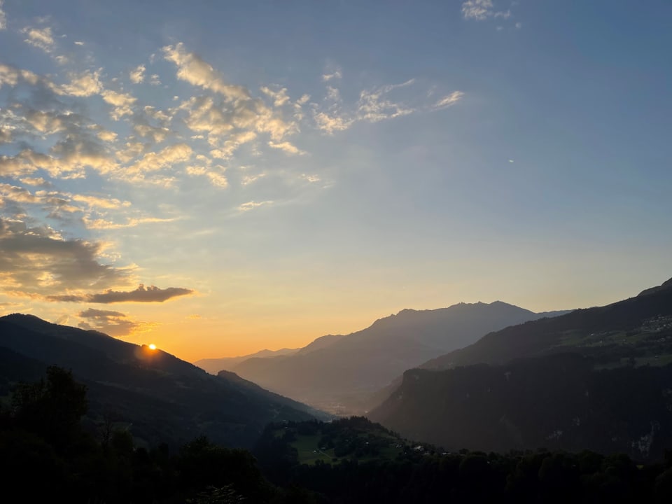 Sonnenuntergang über einem Bergtal mit bewölktem Himmel.