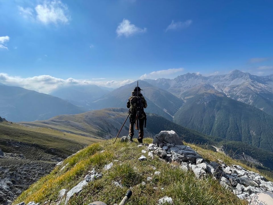 Ein Jägerin blickt auf einer Anhöhe auf die umliegenden Berge im Unterengadin.