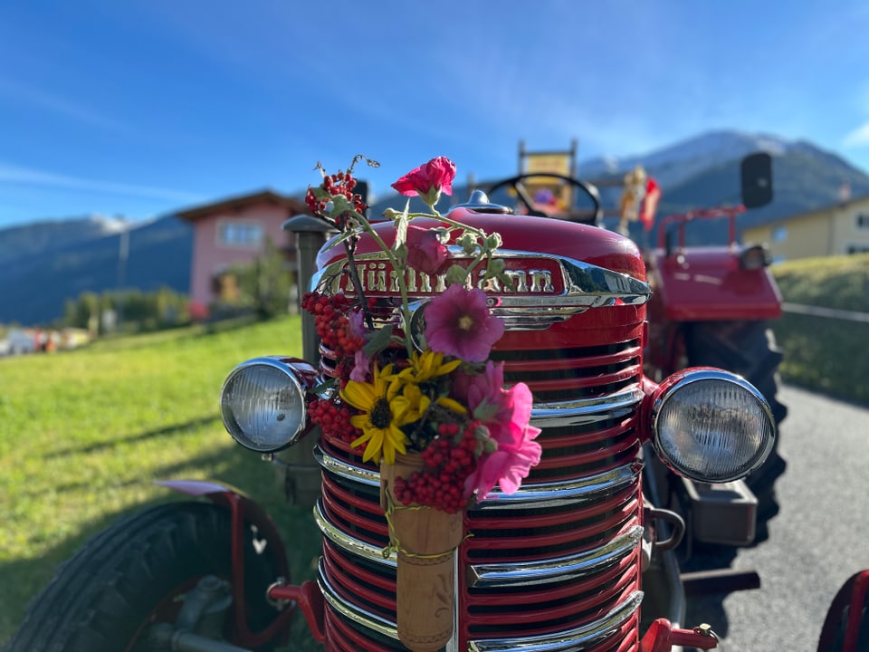 Roter Traktor mit Blumendekoration vor Berglandschaft.