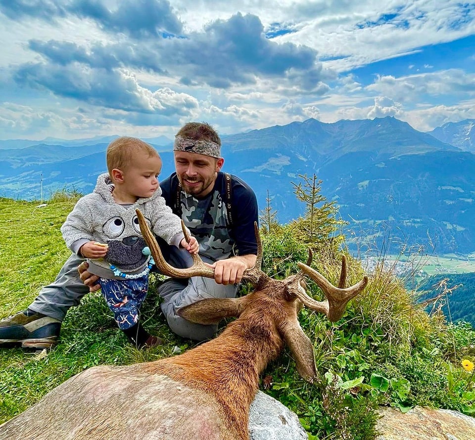 Vater und Kind neben einem erlegten Hirsch auf einem Berg.