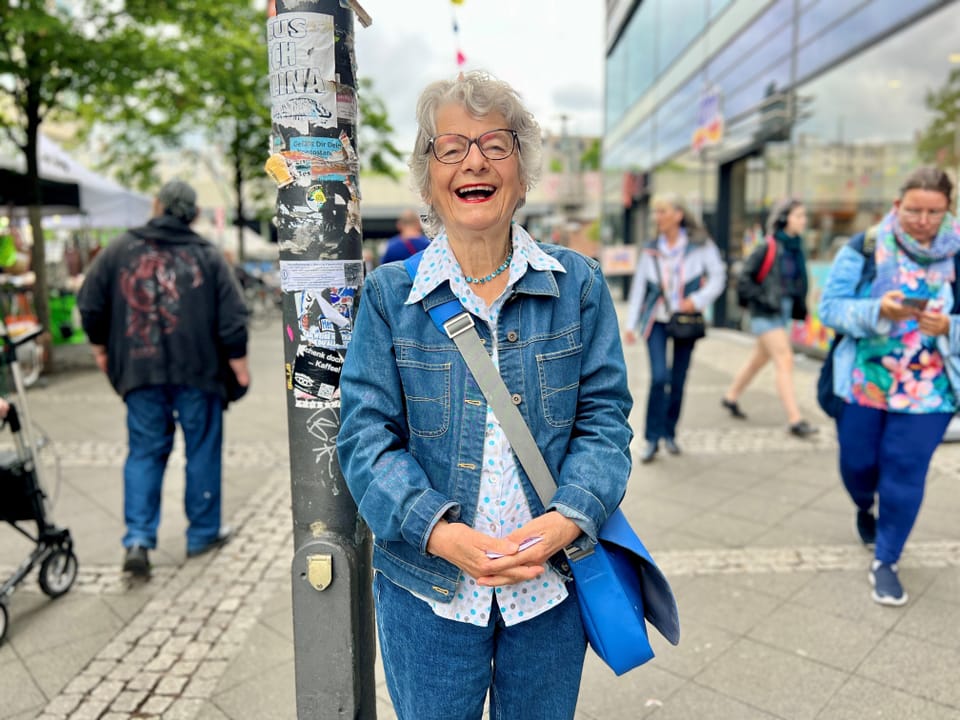 Lachende ältere Frau in einer Jeansjacke, die auf dem Bürgersteig steht.
