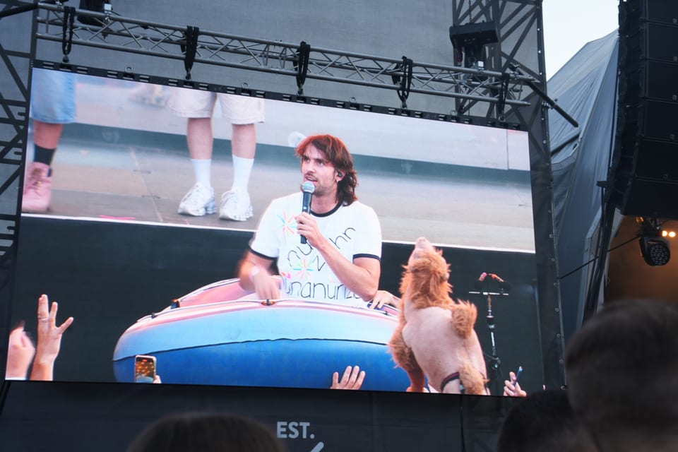 Mann sitzt in einem Schlauchboot auf der Bühne bei einem Konzert, auf der Videoleinwand am Open Air Lumnezia 2024.