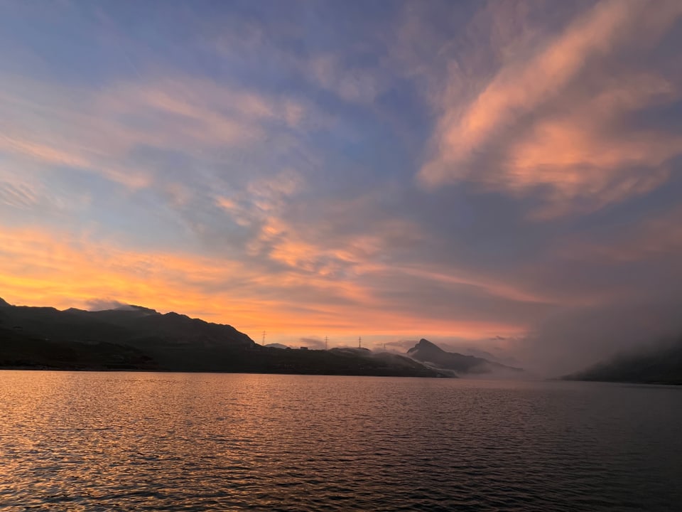 Bergsee bei Sonnenuntergang mit bewölktem Himmel.