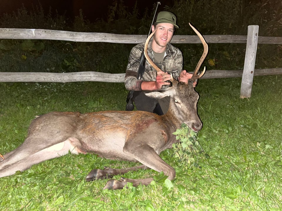 Jäger posiert nachts mit erlegtem Hirsch vor Holzzaun.