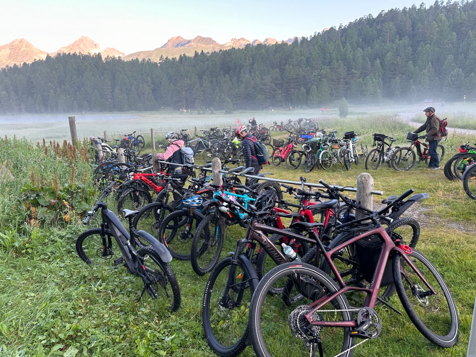 Zahlreiche Fahrräder in einem Nebelfeld auf einem Feld mit Bergen im Hintergrund.